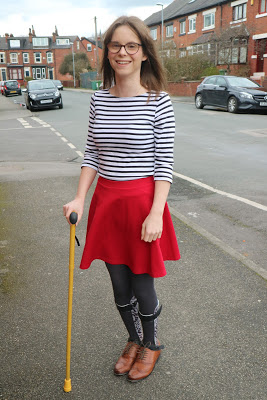 Chloe stood with a yellow walking stick in a red skirt and a white top